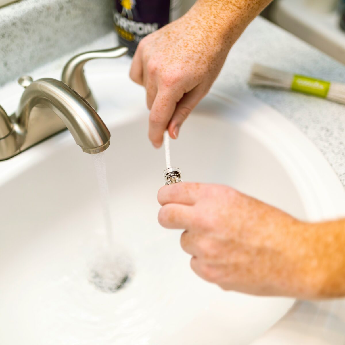 Close-up of a hand turning on a sink faucet with water flowing into the basin