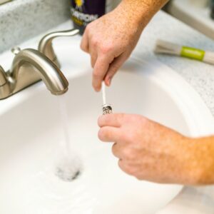 Close-up of a hand turning on a sink faucet with water flowing into the basin